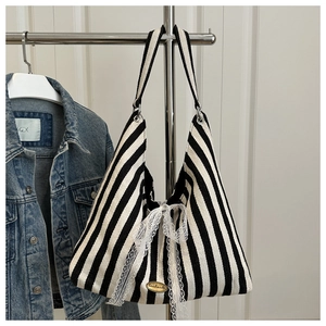 Close-up of black and white striped tote bag with a white lace bow and gold handmade tag