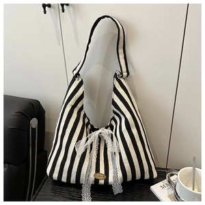 Detail of striped tote bag featuring a large lace bow and a handmade metal emblem