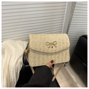 Detail of beige woven crossbody bag featuring a golden bow-knot buckle and straw texture