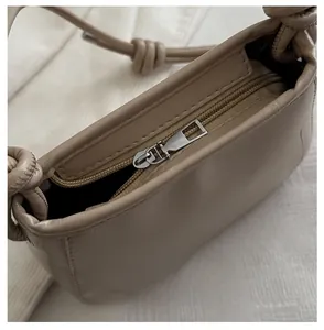 Detail of silver smooth zipper and knotted strap on apricot leather crossbody bag