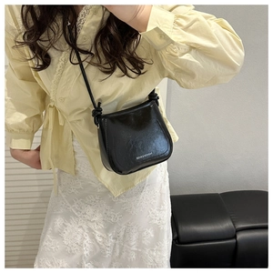 Detail of a sleek black PU leather shoulder bag with chic knot accent and fashion logo