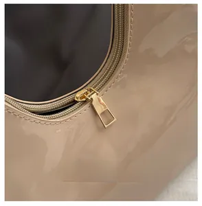 Detailed close-up of premium smooth golden zipper on beige patent leather handbag