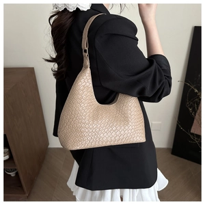 Close-up of beige woven texture hobo bag worn by a model in a minimalist setting