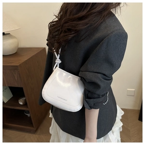 Close-up of a white patent leather shoulder bag with a knotted strap detail worn by a model