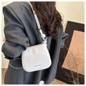 Close-up of white minimalist shoulder bag with unique knotted rope strap detail on model