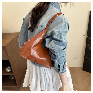 Brown patent leather shoulder bag styled with a denim jacket and white pleated skirt