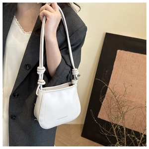 White minimalist shoulder bag with unique knotted strap shown on model in office wear