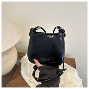 Detail of glossy black mini handbag featuring printed fashion text and knot shoulder strap