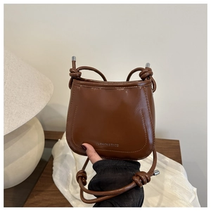 Detail view of the brown patent leather bag with a knotted strap and embossed logo