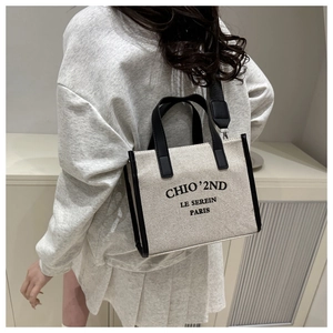 Detail view of canvas tote bag with black wide shoulder strap and printed logo lettering