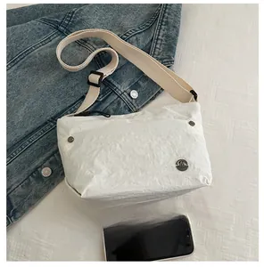 White crossbody bag with crinkled texture shown next to a smartphone for size reference