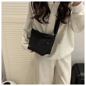 Close-up of black pleated nylon crossbody bag featuring front zip pocket and round logo