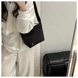 Close-up of black nylon crossbody bag with silver hardware and wide fabric shoulder strap
