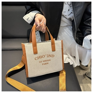 Detail of canvas crossbody bag with yellow strap and Parisian text on beige fabric