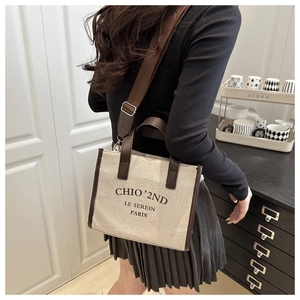 Rear view of a stylish beige canvas tote bag with brown leather trim and fabric strap
