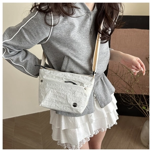 Close-up of white pleated crossbody bag with woven strap and small black logo detail