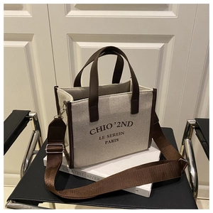Detail of canvas tote bag featuring brown leather trim and detachable wide fabric shoulder strap