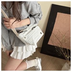 Detail of white textured crossbody bag featuring pleated fabric and silver metal buckle