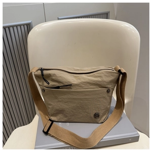 Close-up of khaki pleated crossbody bag with metal logo detail and wide fabric strap