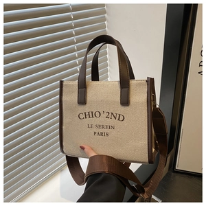 Détail d'un cabas en toile avec poignées en cuir marron et logo dans un décor urbain