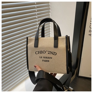 Détail du sac cabas en toile avec bordure en cuir noir et logo devant un mur minimaliste