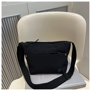 Close-up of black nylon crossbody bag featuring front pockets and circular metal logo