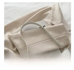 Gros plan d'un sac à main en cuir blanc avec boucle nœud argentée sur fond de veste beige