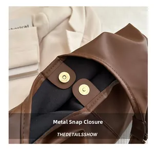 Detail of the golden magnetic buckle closure on a brown leather tote shoulder bag