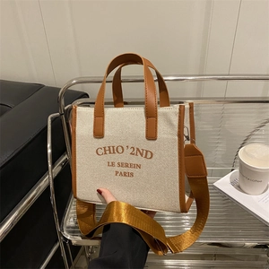 Beige canvas and brown leather tote bag with shoulder strap on a display stand