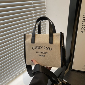 Minimalist beige canvas tote bag with black leather trim and wide crossbody strap