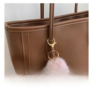 Pink furry monster bag charm with gold clasp detail on a brown leather tote bag