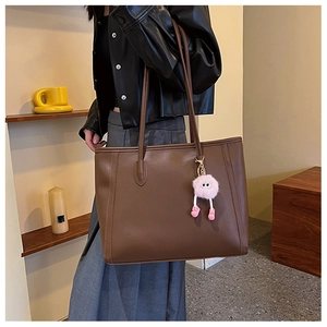Detail view of deep brown minimalist leather tote bag with cute pink plush charm accessory