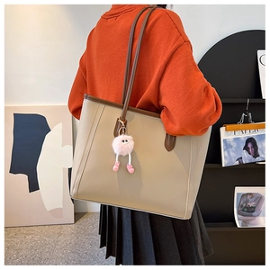 Detail of a large beige leather tote bag with brown straps and a pink monster charm pendant