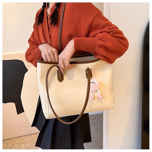 Close-up of beige tote bag with dark brown straps and pink plush pendant accessory