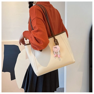 Side view of woman carrying a large beige leather tote bag with brown trim and plush charm