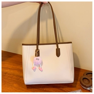 Detail view of cream tote bag with brown handles and a pink pompom charm on a wood table