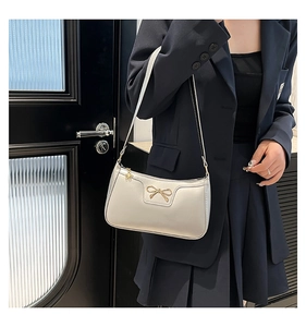 Detail of light beige shoulder bag featuring a gold bow accent and floral zipper charm