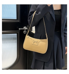 Détail du sac sous le bras en cuir beige avec nœud métallique et fine bandoulière élégante
