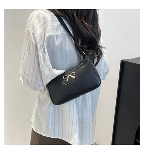Détail du sac baguette en cuir noir mat avec un nœud doré porté par un mannequin femme
