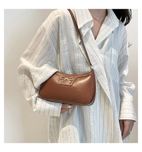 Detail of a brown leather shoulder bag featuring a golden bow metal buckle on a model