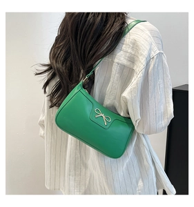Sac à bandoulière vert avec boucle nœud doré porté sur une chemise blanche