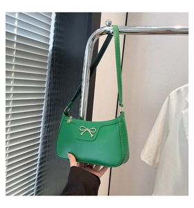 Detail of emerald green leather baguette bag featuring a gold bow accent and flower charm