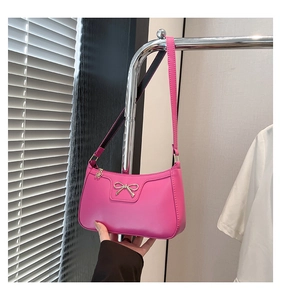 Detail of pink faux leather shoulder bag featuring a metal bow and floral charm