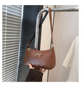 Close-up of caramel faux leather shoulder bag with a metal bow and floral zipper puller