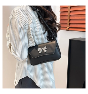 Detail of a black leather underarm bag featuring a silver metal bow accent and slim strap