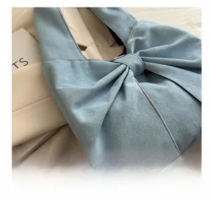 Close-up of light blue denim tote bag with a large bow and decorative brown stitching
