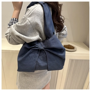 Model wearing a dark blue denim tote bag with a large bow in a cozy indoor setting