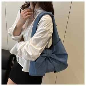 Detail of blue denim shoulder bag featuring a large decorative bow and wide strap