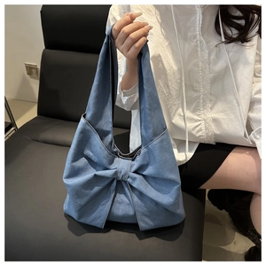Close-up of stylish blue denim tote bag featuring a large decorative bow on a leather sofa