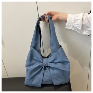 Detail of blue denim tote bag with a large decorative bow handle held by hand